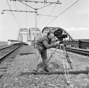 849529 Afbeelding van cineast Herman Wassenaar tijdens het filmen van treinen bij de spoorbrug over het ...